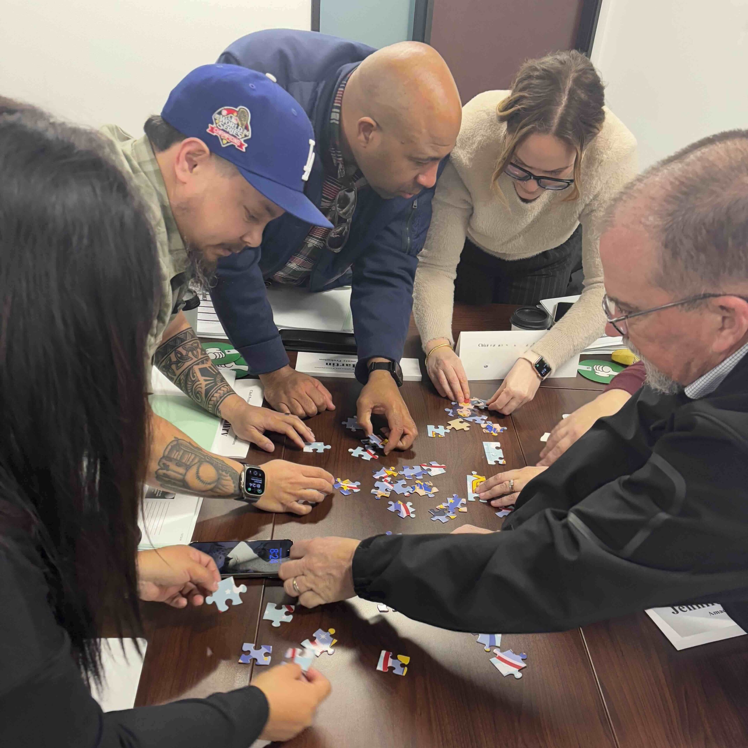 Five people stand around a table working together to put a puzzle together